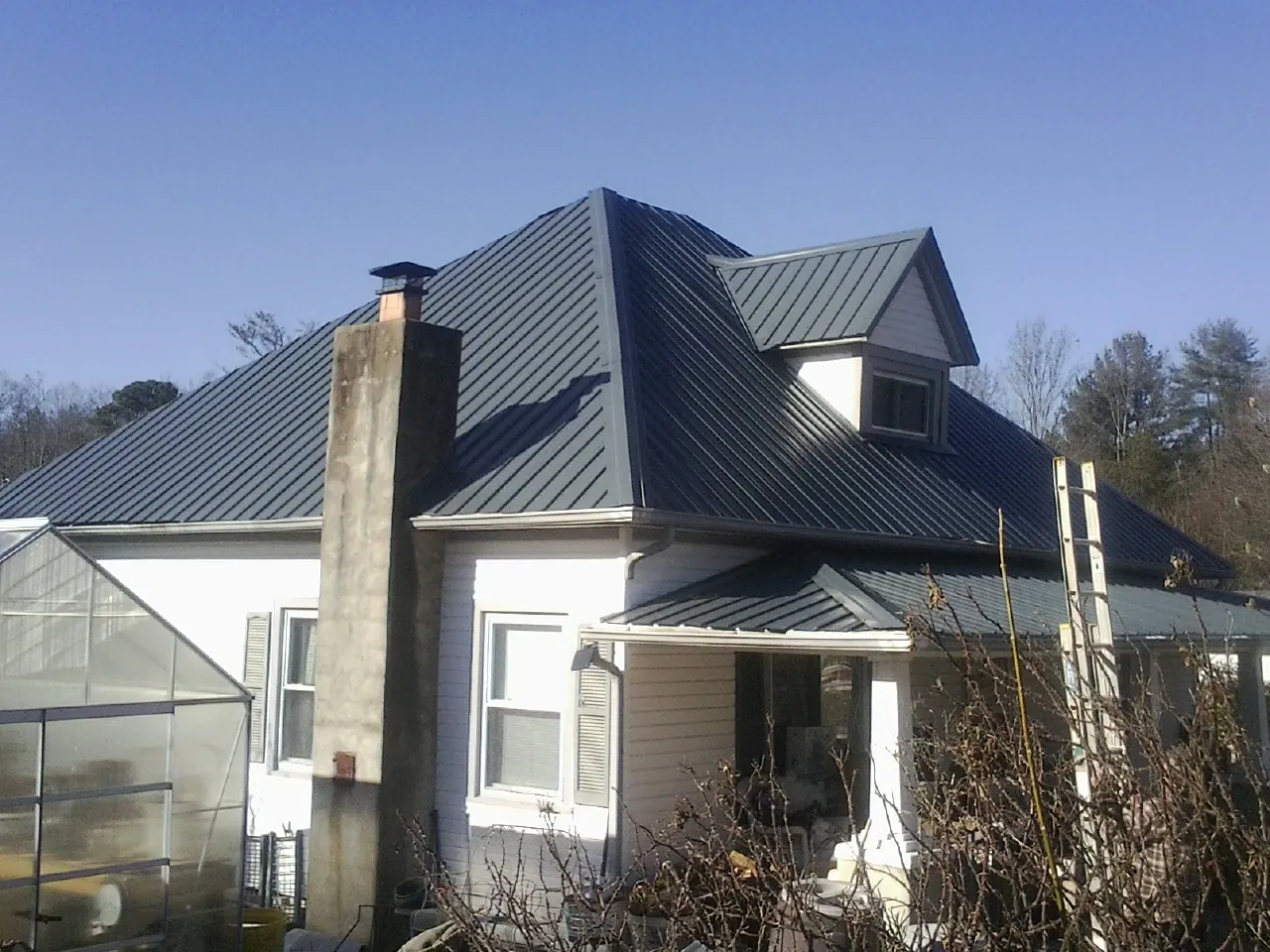 Dark blue standing seam metal roof on a white farmhouse with dormer — Slate & Tile Roof Repair by Roofing Brothers in Commerce
