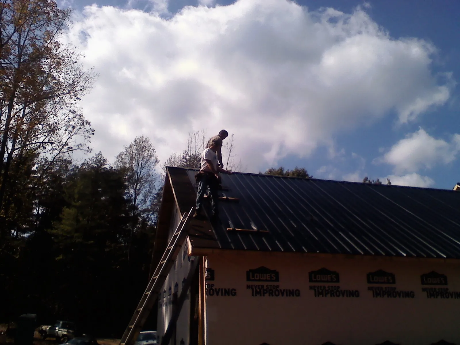 Roofer fastening dark metal panels high against a cloudy sky, from a Roof Inspection job in Commerce